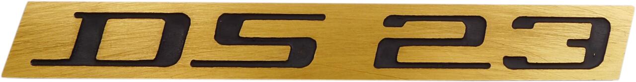 Emblem "DS 23". Aus Aluminium, goldfarbig mit schwarzer Schrift.